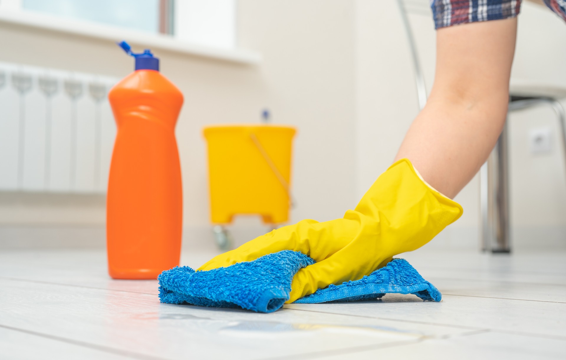 Mujer con guantes limpiando piso. Producto de limpieza y cuidado para laminados y pavimentos. Manos femeninas con guantes amarillos Limpie el piso de madera con un paño azul de microfibra